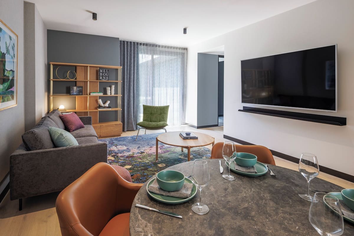 Una sala de estar moderna con un sofá, una mesa de comedor con cuencos y copas de vino, un televisor montado en la pared y una estantería.