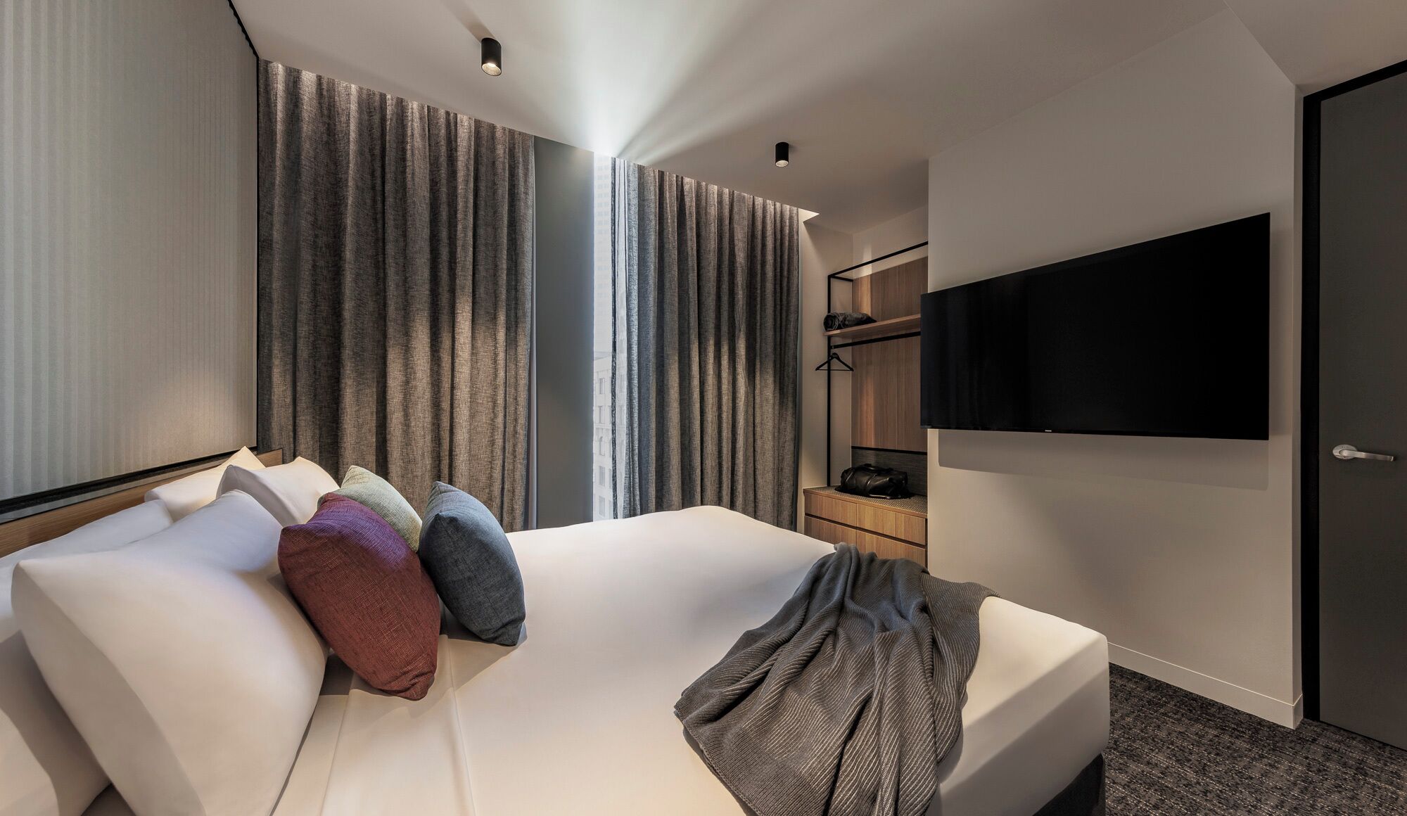 A modern hotel room with a large bed, a flat-screen TV, and a wardrobe.