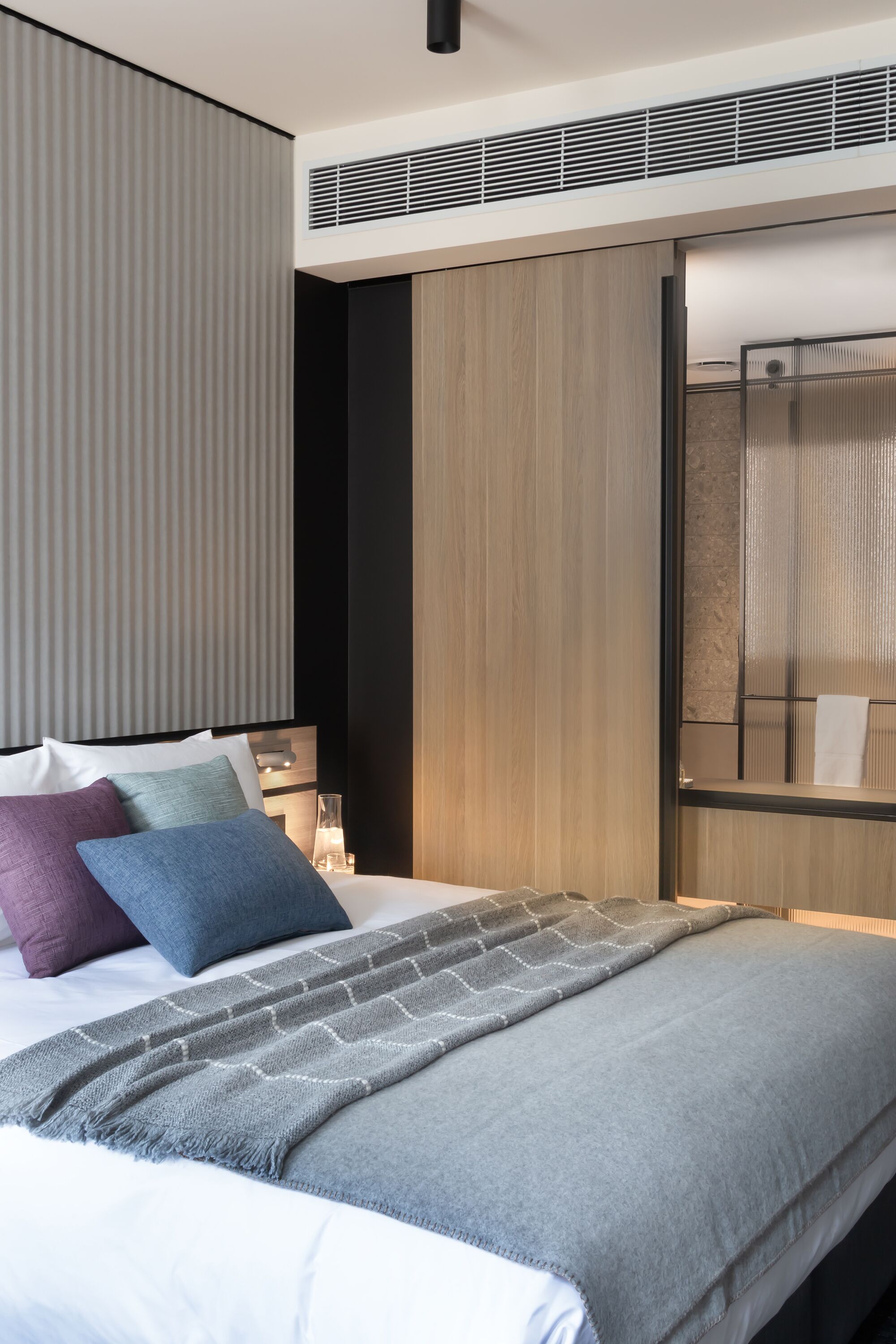Quarto de hotel moderno com cama, mesa de cabeceira, espelho e guarda-roupa.