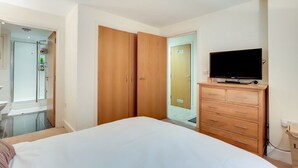 Habitación de hotel con cama, armario de madera, televisor y baño a la vista a través de una puerta abierta.