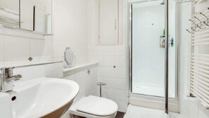 Un baño moderno con lavamanos, inodoro y ducha con mampara de vidrio.