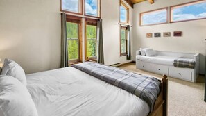 Relax in a cozy bedroom with a large bed, plaid bedspread, and storage bench beneath a window with a view of lush greenery.