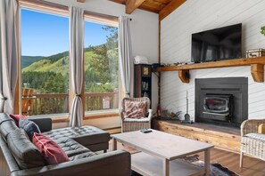 Relax by the fireplace with a scenic view of the forested hillside.