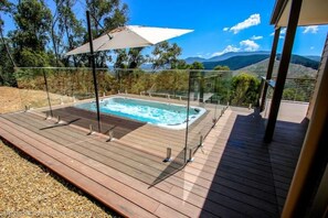 Relax in a hot tub on a deck surrounded by trees and distant hills.