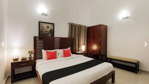 Una habitación de hotel con una cama grande, cabecero de madera, mesitas de noche, un banco y un armario.