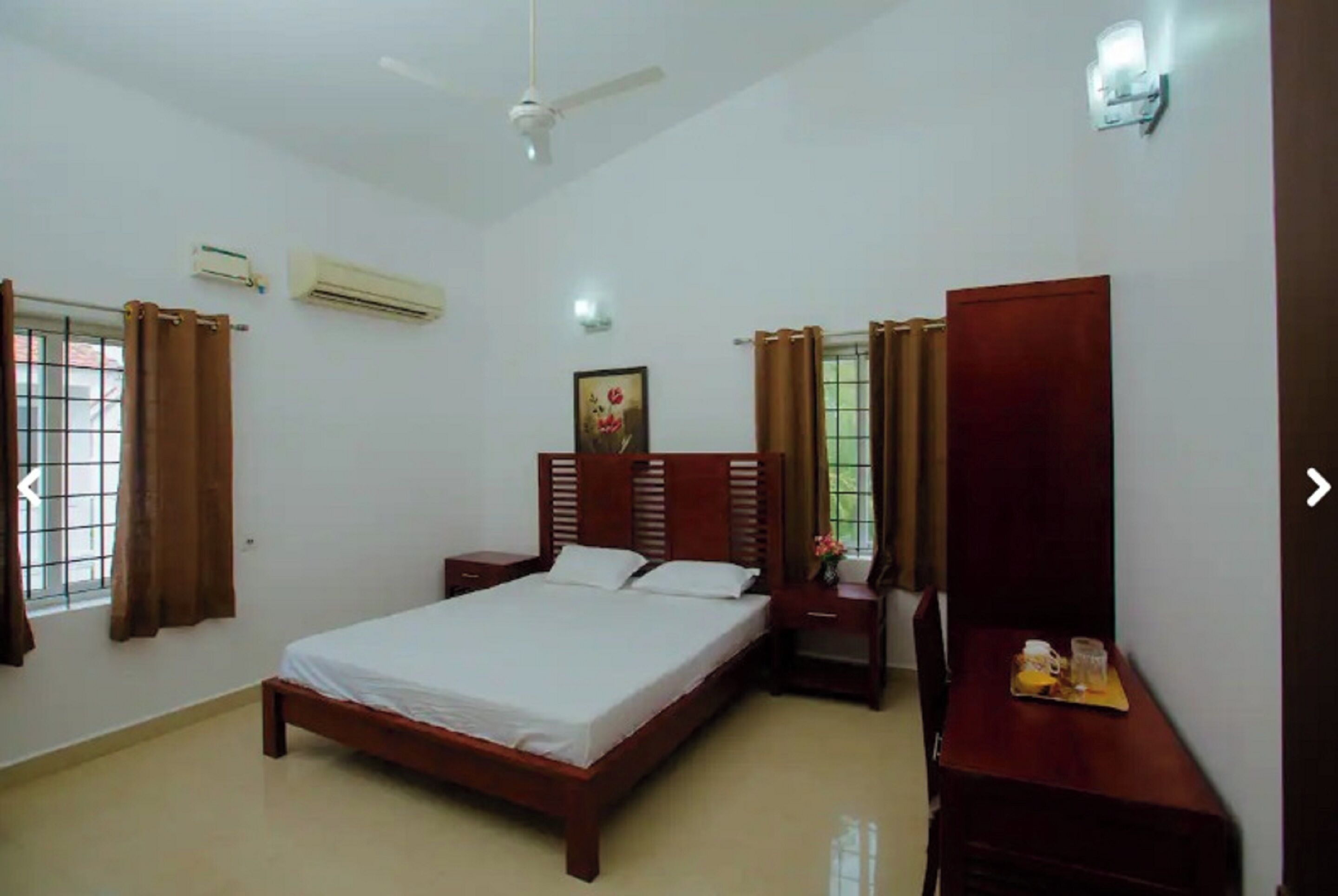 A bedroom with a bed, bedside tables, a wardrobe, an air conditioning unit, and a ceiling fan.