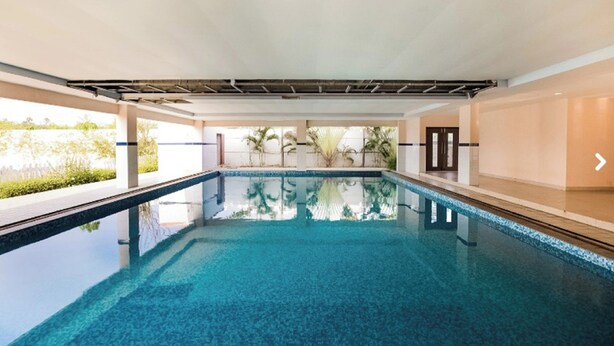 Una amplia piscina interior con agua cristalina y azul, rodeada de paredes y un techo con vigas a la vista.