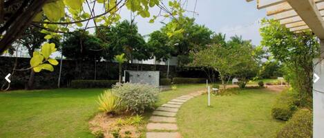 A garden with a stone pathway, various plants, and a white building in the background.