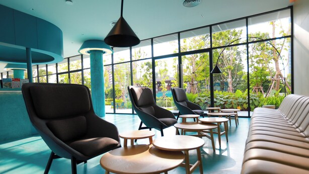 Un espace de détente intérieur moderne, doté d’un canapé, de fauteuils et de petites tables, et agrémenté de grandes fenêtres offrant une vue sur la verdure.