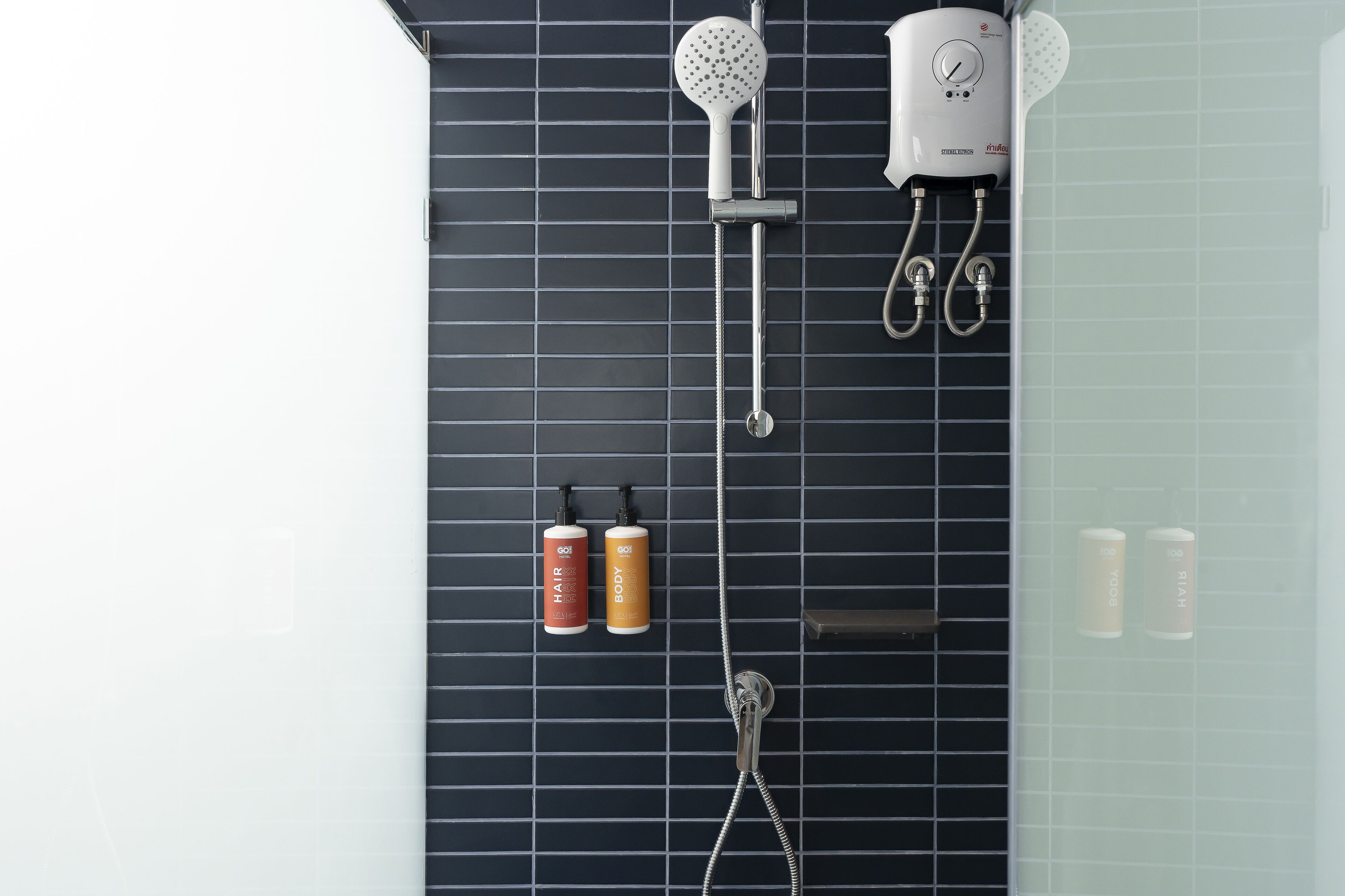 A modern bathroom with a black tiled wall, a handheld showerhead, a wall-mounted faucet, and two bottles of shampoo and conditioner.