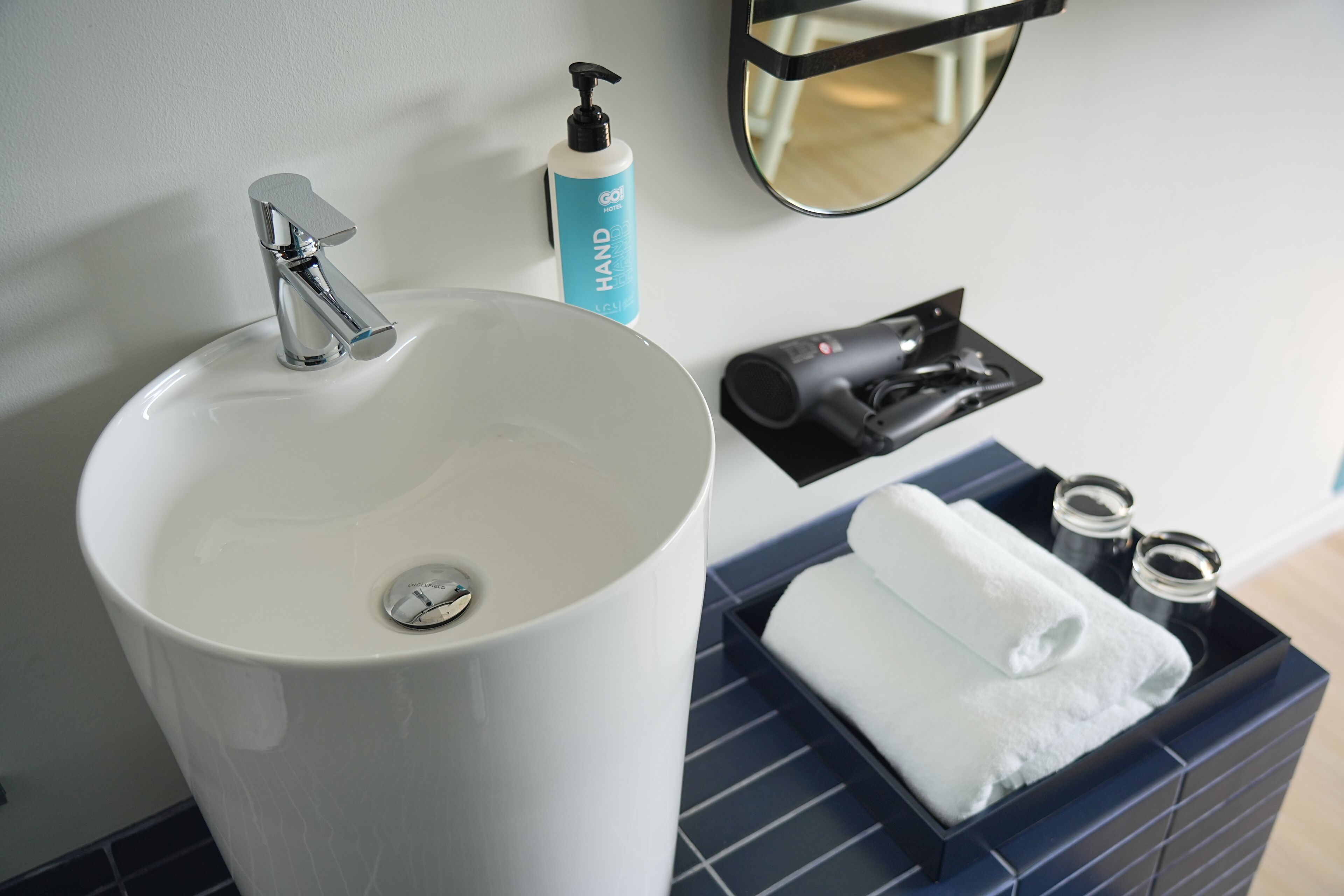 Une salle de bain avec un lavabo blanc, un distributeur de savon liquide, un sèche-cheveux et un porte-serviettes.