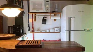 A kitchen with a wooden countertop, a microwave, a refrigerator, and a hanging pot rack. - Ibirapuera Park House (São Paulo)
