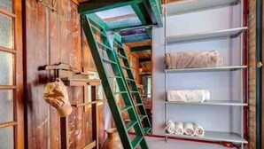 A rustic room with wooden walls, a green ladder, shelves with towels, and a hanging bag. - Ibirapuera Park House (São Paulo)