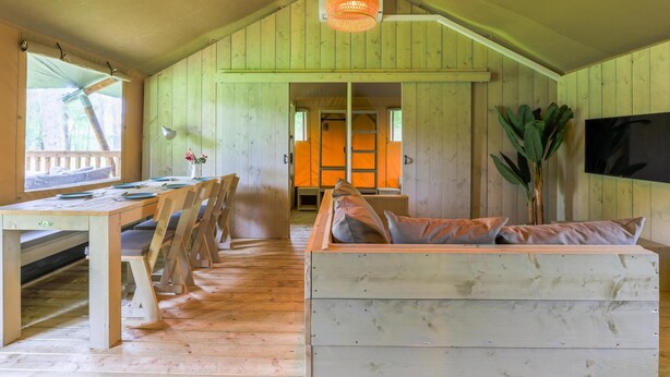 Une cabane en bois comprenant un coin repas, un canapé et un téléviseur fixé au mur.