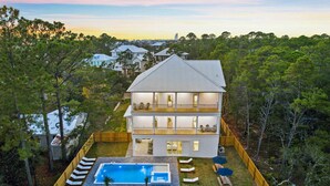 A two-story house with a swimming pool, multiple balconies, and a view of surrounding trees.