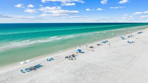 A beach with clear turquoise waters, white sand, and a few umbrellas and beach chairs.