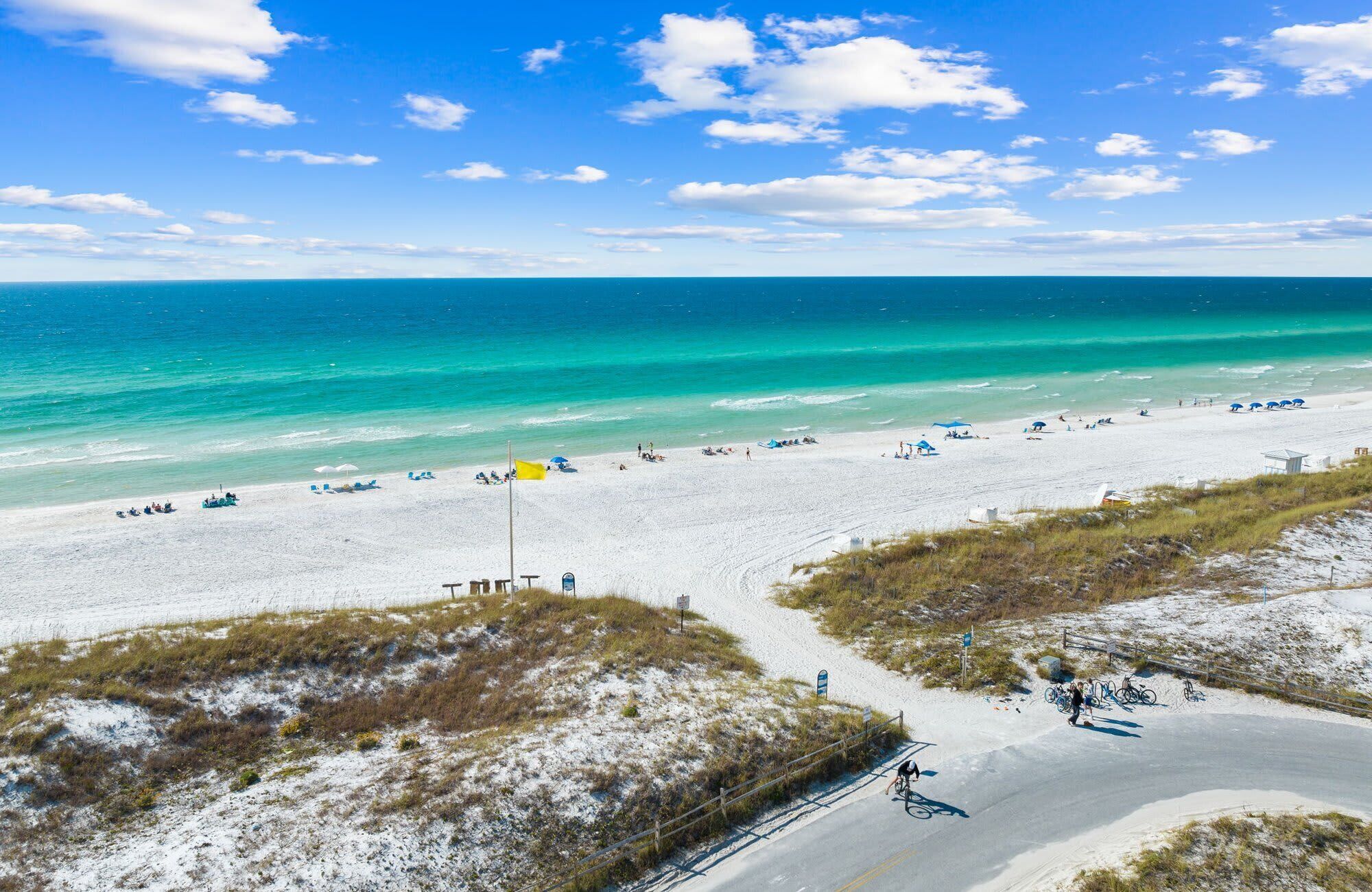 A beach with a clear sky, a sandy shore, and a few people and bicycles.