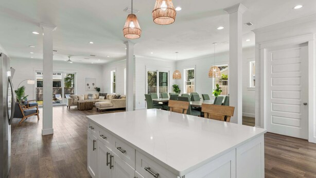 A spacious kitchen with a large island, pendant lighting, and a dining area with green chairs.