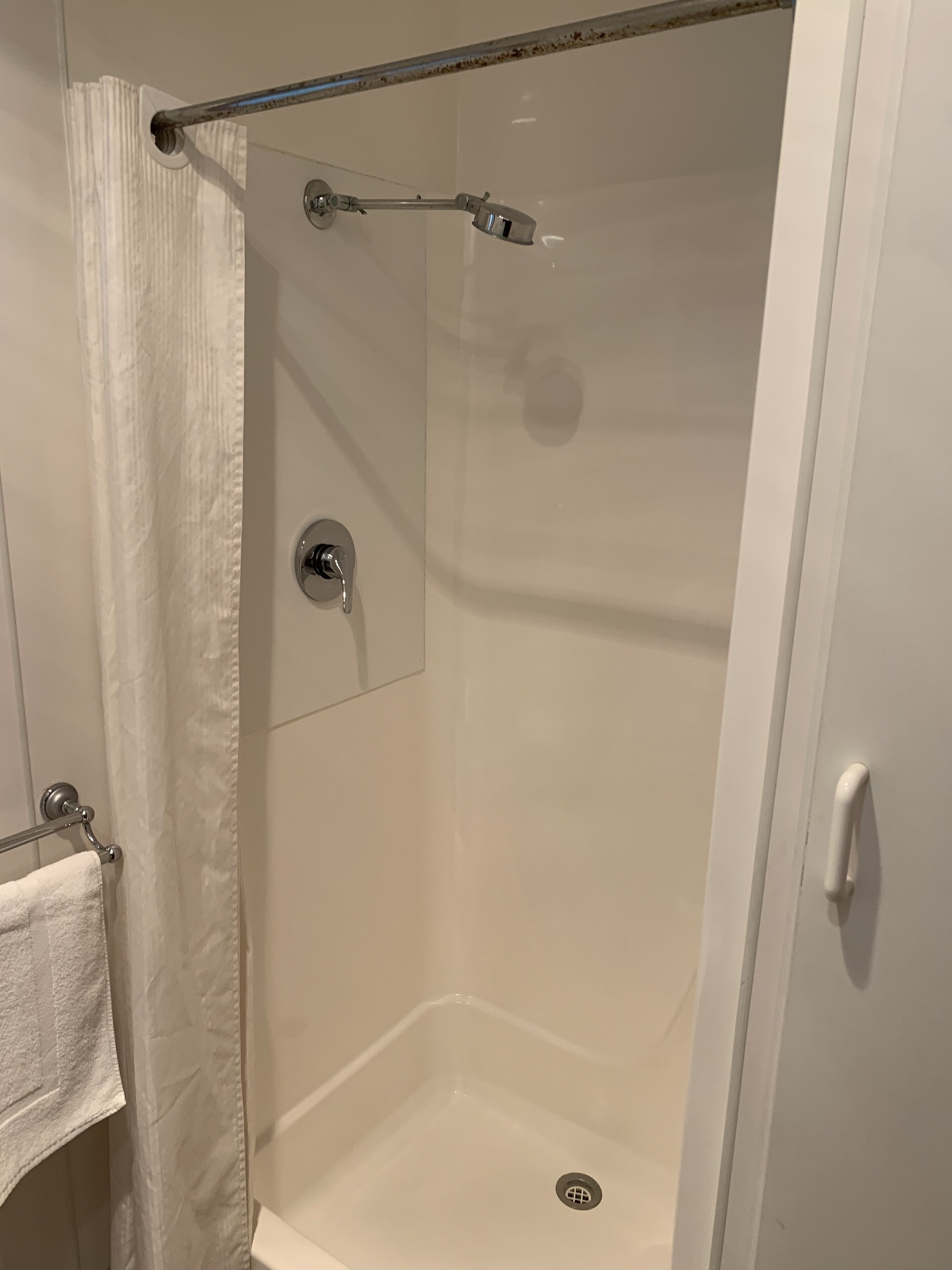 Una ducha a ras de suelo con puerta de cristal, cabezal de ducha y un rociador de mano.