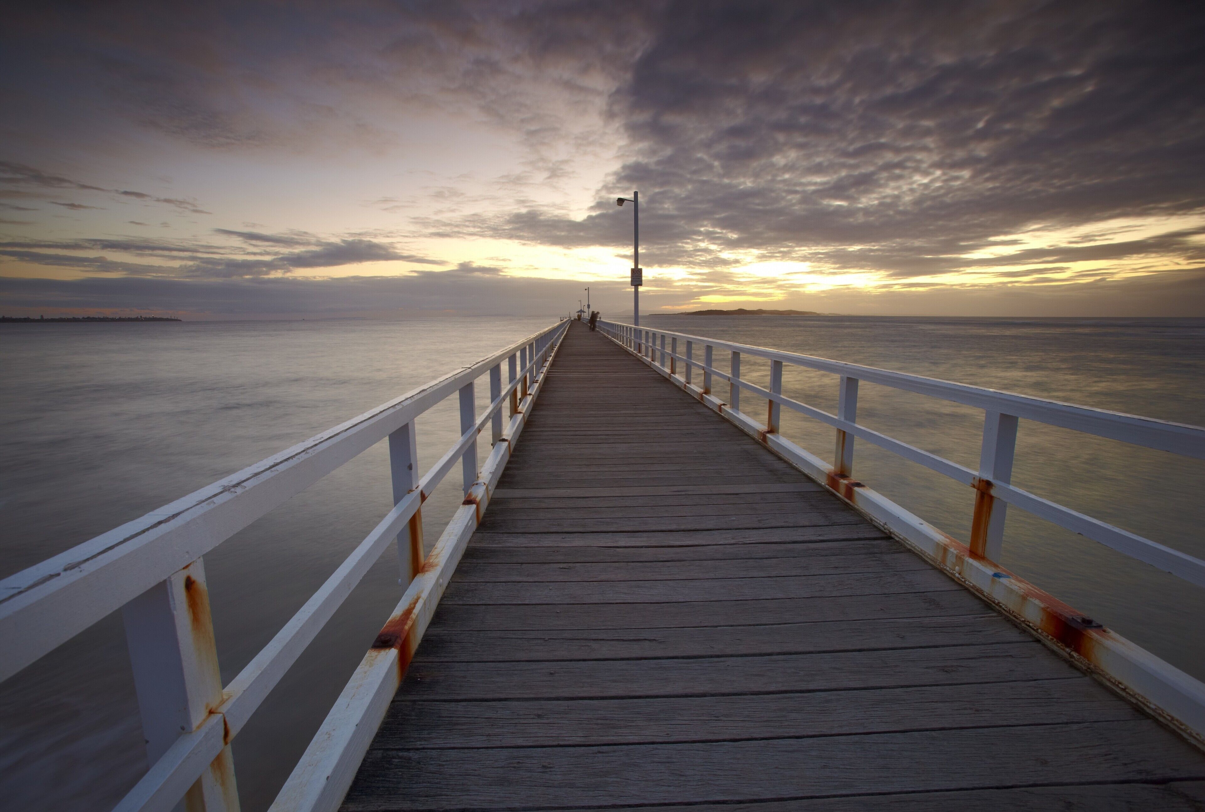 A wooden pier extending into calm waters under a cloudy sky.