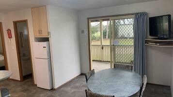 Una cocina compacta con refrigerador, una mesa de comedor con sillas, un televisor en un mueble bajo y una puerta corrediza de vidrio que da a un balcón.