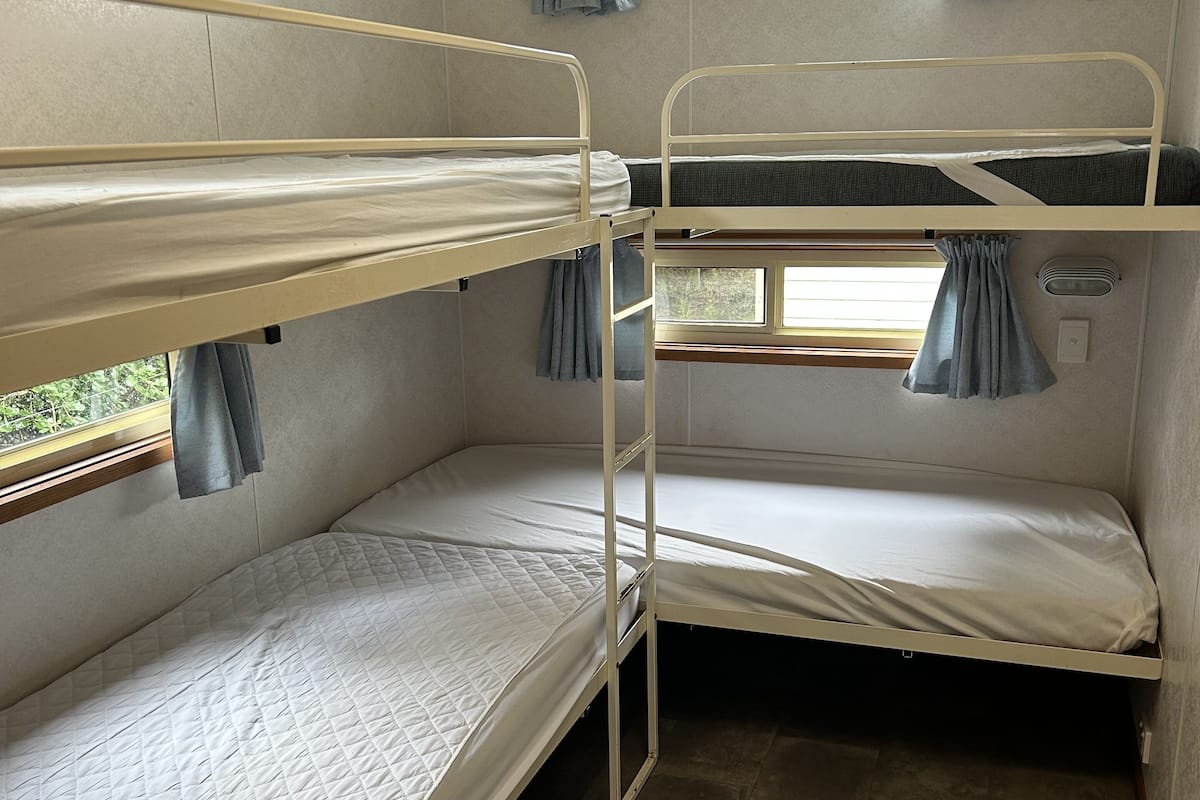 A bunk bed room with two beds, a window with curtains, and a ventilation unit.