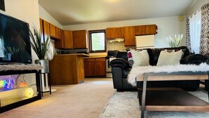 A living room with a sofa, a TV, and a kitchen in the background. - Cozy house close to all shops/malls, 7 minutes to fort wainwright  (Fairbanks)