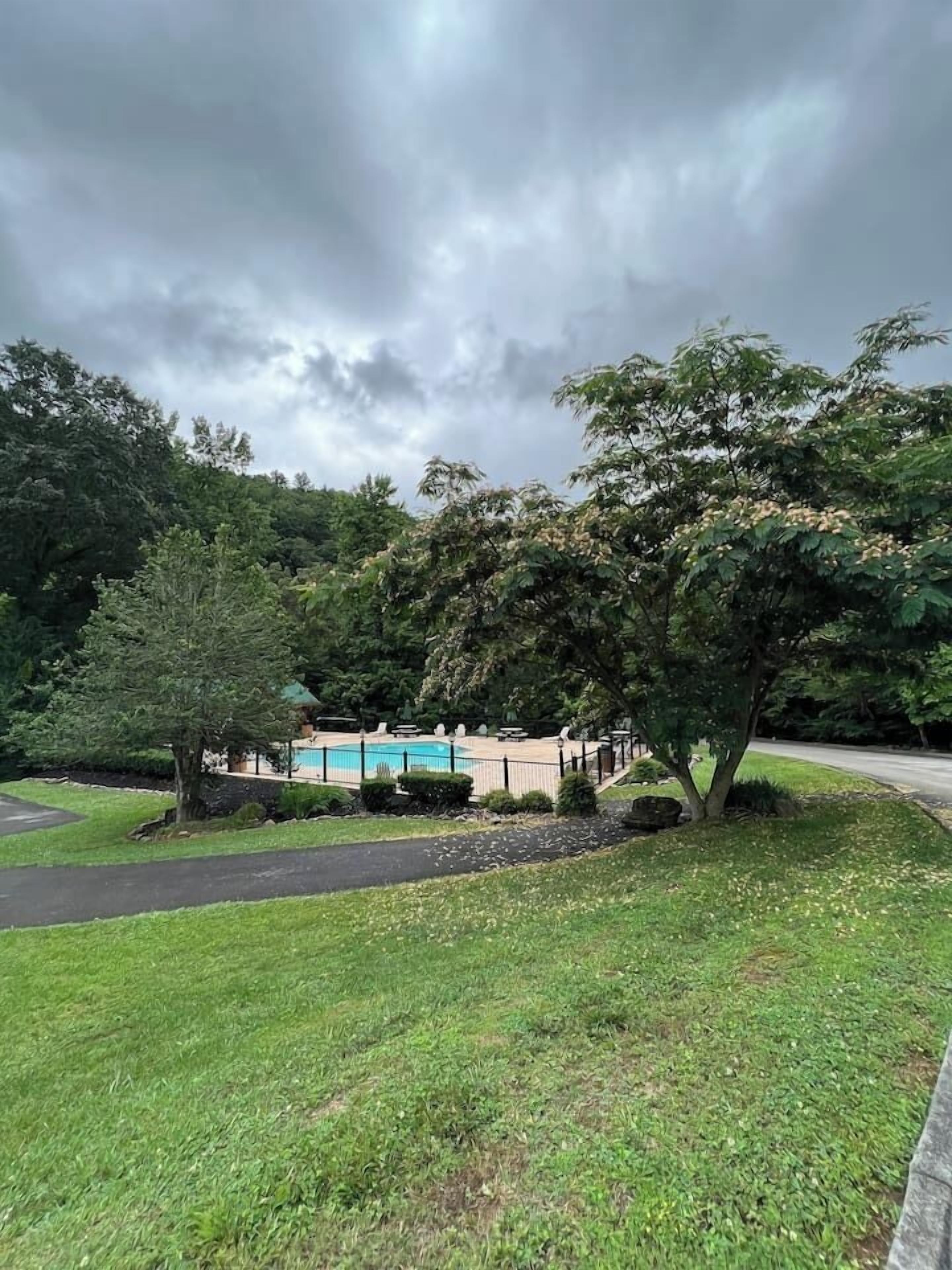 A residential area with a swimming pool, surrounded by trees and a paved pathway.