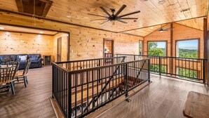 Een ruim interieur van een blokhut, met een houten vloer, een balkon met balustrade en een plafondventilator.