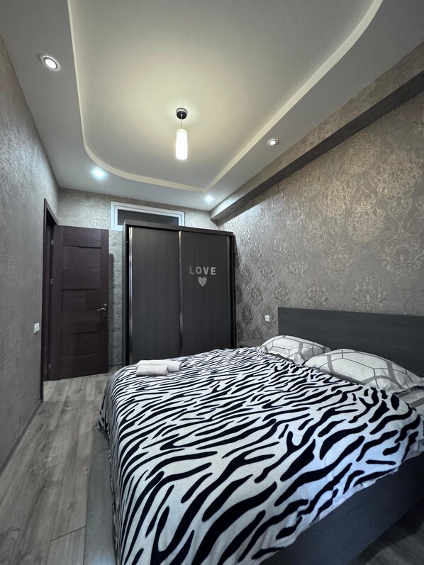 A bedroom with a zebra-patterned bedspread, a dark wooden wardrobe with a 'LOVE' sign, and a textured wall.