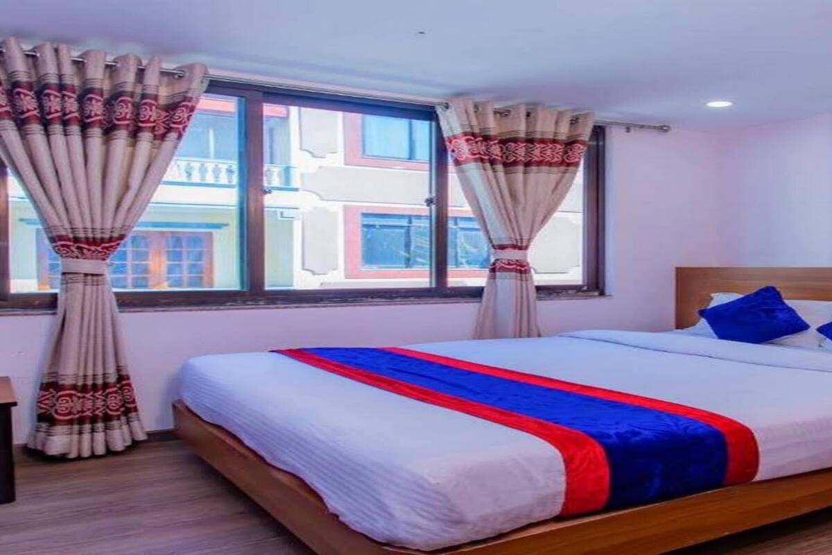 A hotel room with a large bed, wooden headboard, and a window with curtains.