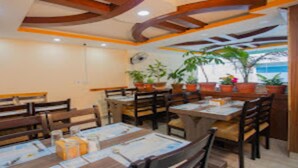 Un restaurante con mesas y sillas de madera, plantas en macetas y un ventilador en el techo.