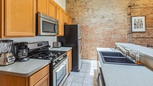 A kitchen with wooden cabinets, a stainless steel refrigerator, a microwave, a stove, and a sink. - The Victor 3 - Cleveland's Urban Lodge (Cleveland)
