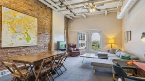 A spacious room with a large wooden dining table, a leather sofa, and a comfortable armchair. A map is displayed on the wall, and there is a television in the corner. - The Victor Full - Cleveland's Urban Lodge - Sleep 51! (Cleveland)