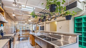A kitchen with stainless steel appliances, hanging pots, and potted plants. - The Victor Full - Cleveland's Urban Lodge - Sleep 51! (Cleveland)