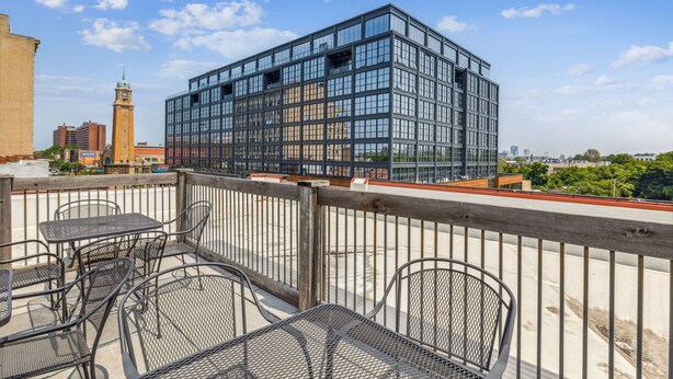 A modern building with large windows, a balcony with metal chairs, and a clock tower in the background. - The Victor Full - Cleveland's Urban Lodge - Sleep 51! (Cleveland)