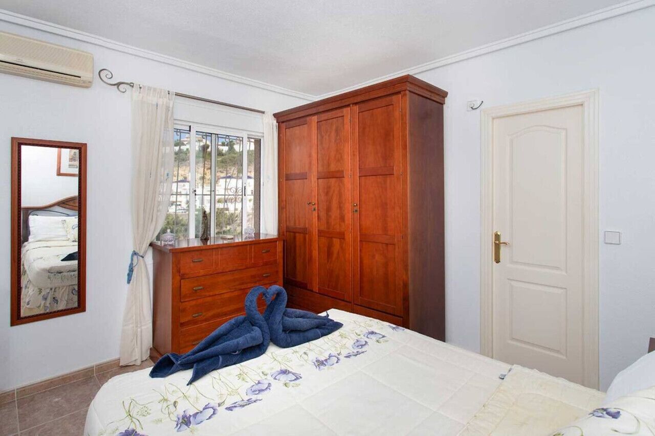 A bedroom with a bed, a wooden wardrobe, a window with curtains, and a door.
