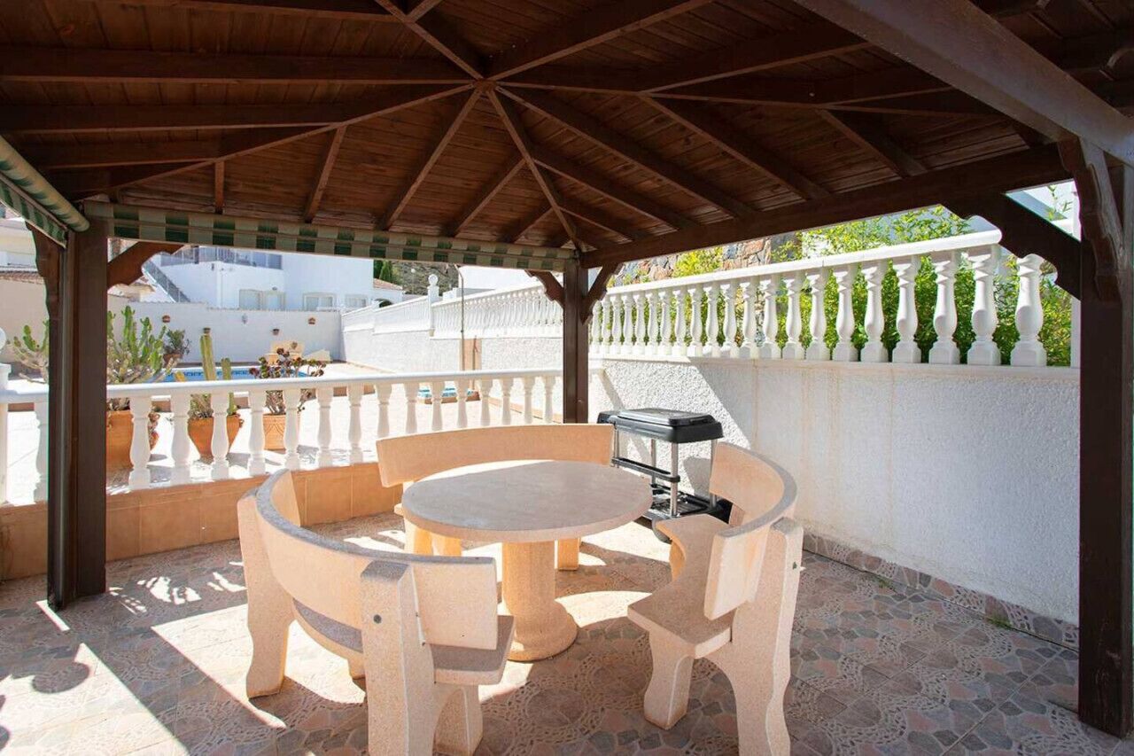 Une terrasse extérieure dotée d’une pergola en bois, d’une table ronde et de deux chaises.