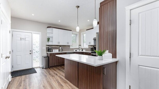 A modern kitchen with white cabinetry, a central island, pendant lighting, and a wooden accent wall. - Central. New Duplex. Sleeps 6. 3 bed/2 bath. (Edmonton)