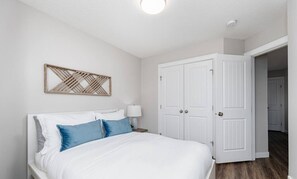 Ein Schlafzimmer mit einem Bett, einem Nachttisch, einer Wanddekoration und einer weißen Tür.