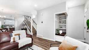 A modern living room with a brown leather sofa, white armchair, and a staircase leading to a kitchen. - Central. New Duplex. Sleeps 6. 3 bed/2 bath. (Edmonton)