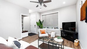 A modern living room with a sofa, coffee table, TV, and a ceiling fan. - Central. New Duplex. Sleeps 6. 3 bed/2 bath. (Edmonton)