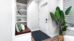 A clean, white hallway with a built-in bench, a large potted plant, and a door with a window. - Central. New Duplex. Sleeps 6. 3 bed/2 bath. (Edmonton)