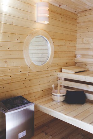 Una sala de sauna con paredes de madera, un tragaluz circular, un banco de madera y un calentador de sauna.