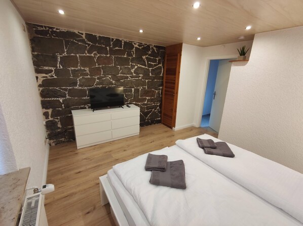 Un dormitorio con pared de piedra, cómoda blanca, televisor y dos camas con toallas.