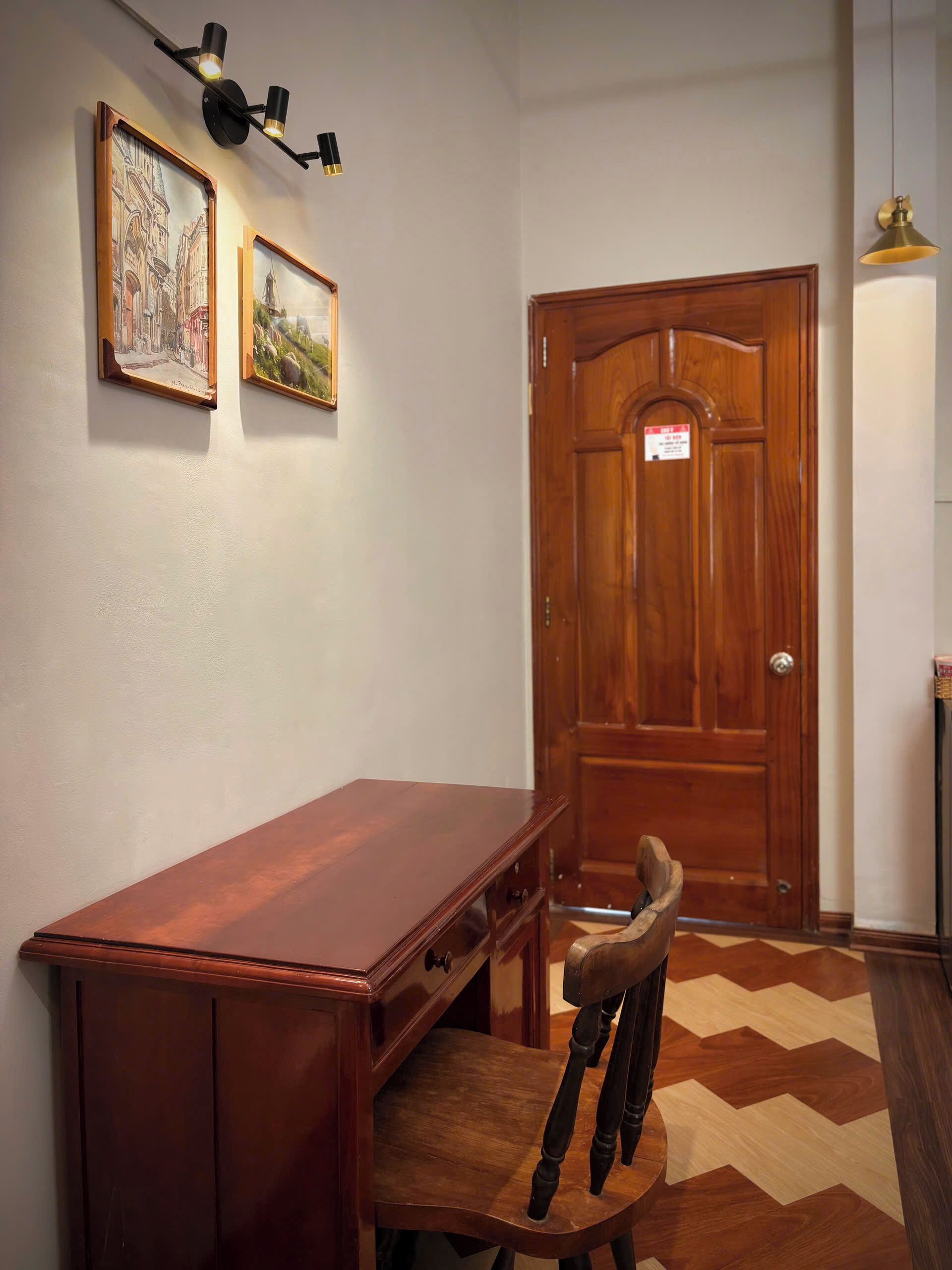 A wooden desk with a chair, a wooden door, and two framed pictures on the wall.