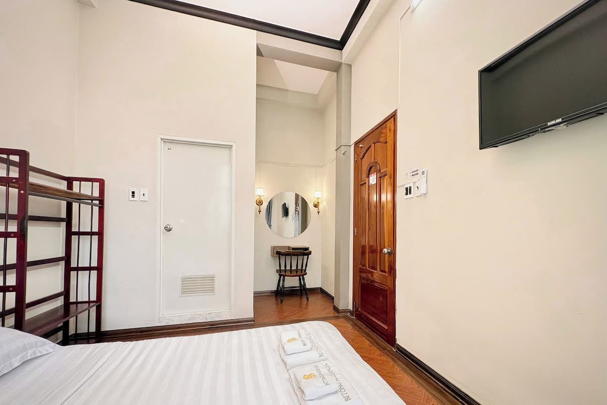 A hotel room with a bed, a wooden bench, a mirror, and a TV mounted on the wall.