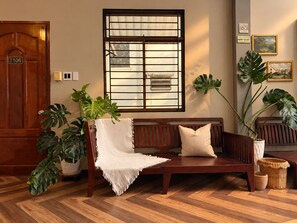 A wooden bench with a white throw blanket and cushion, a potted plant, and a window with a metal grid. - Bê Tông Residences Homestay (Can Tho)
