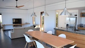A modern kitchen with a large island, white chairs, and pendant lighting.