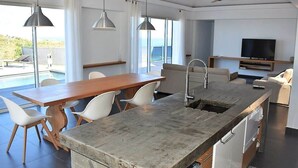 A modern kitchen with a large island, dining area, and a TV.